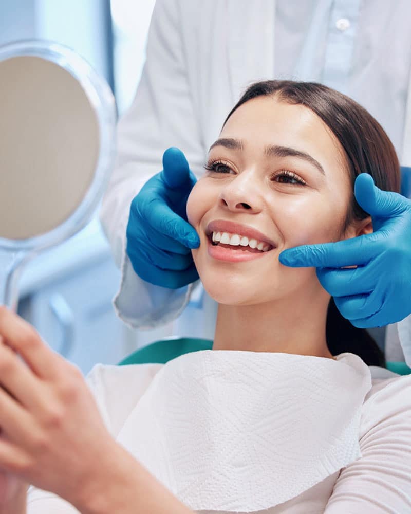 Smiling woman sitting in a dental chair with a mirror.