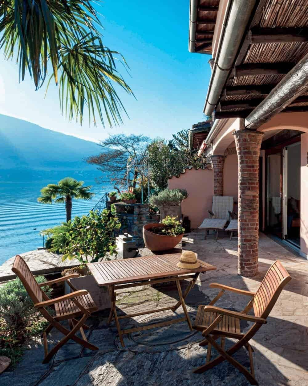 Tela vista di una terrazza con vista lago, piante, arredi in legno e atmosfera rilassante.