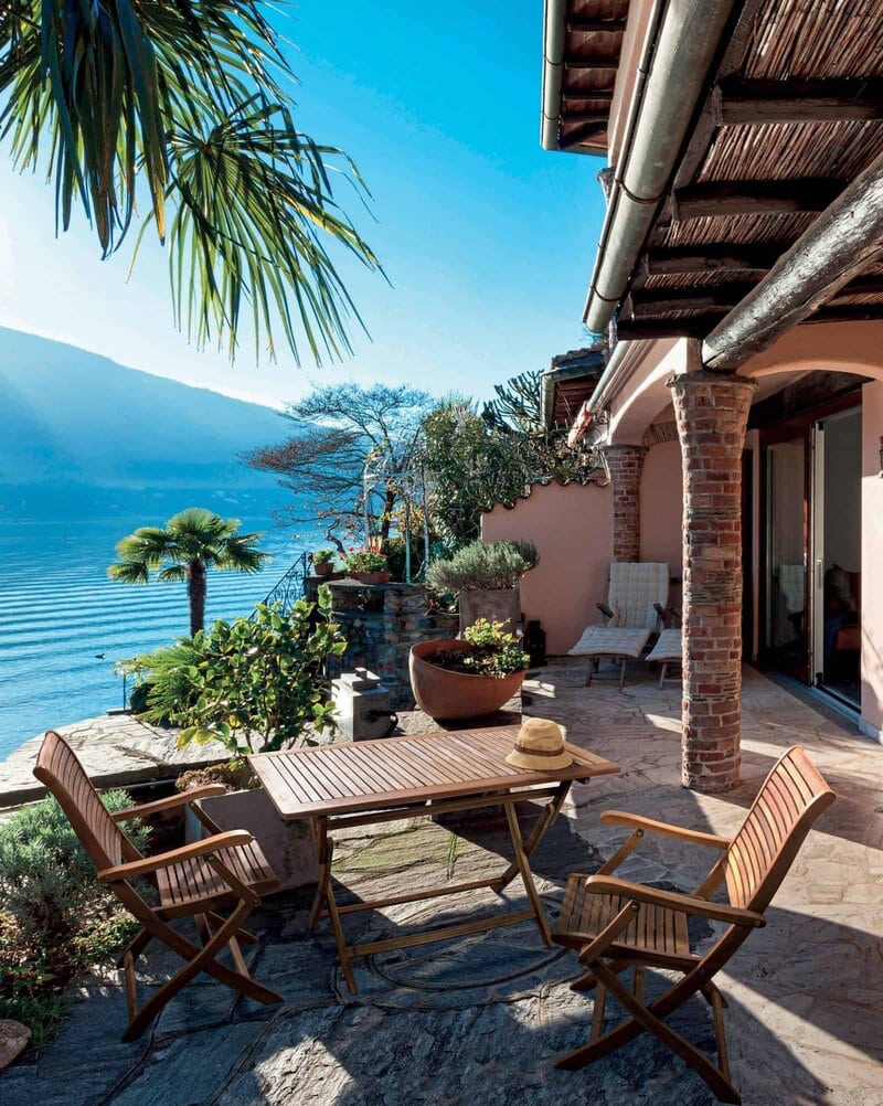 Tela vista di una terrazza con vista lago, piante, arredi in legno e atmosfera rilassante.