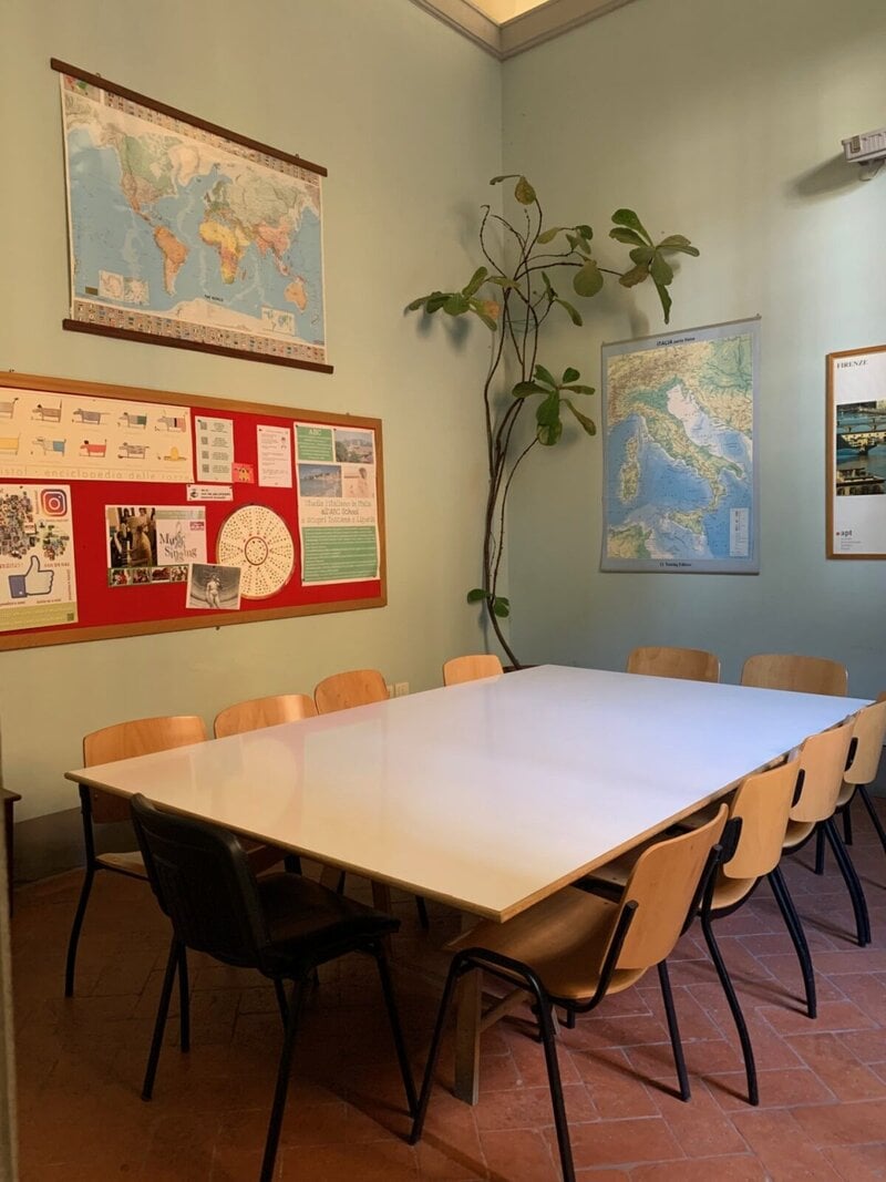 Ein gemütlicher Klassenraum mit einem großen Tisch, umgeben von Stühlen, Weltkarten und einem Infoboard an der Wand.