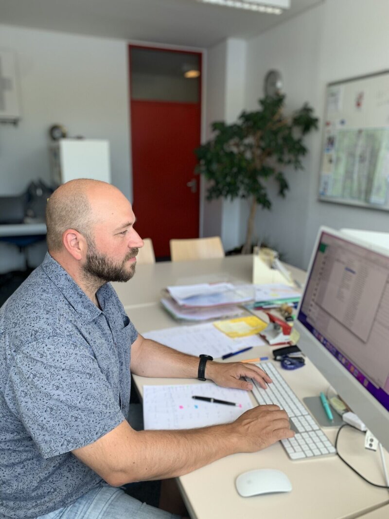 Mitarbeiter arbeitet konzentriert am Schreibtisch mit Computer und Dokumenten in einem modernen Büro