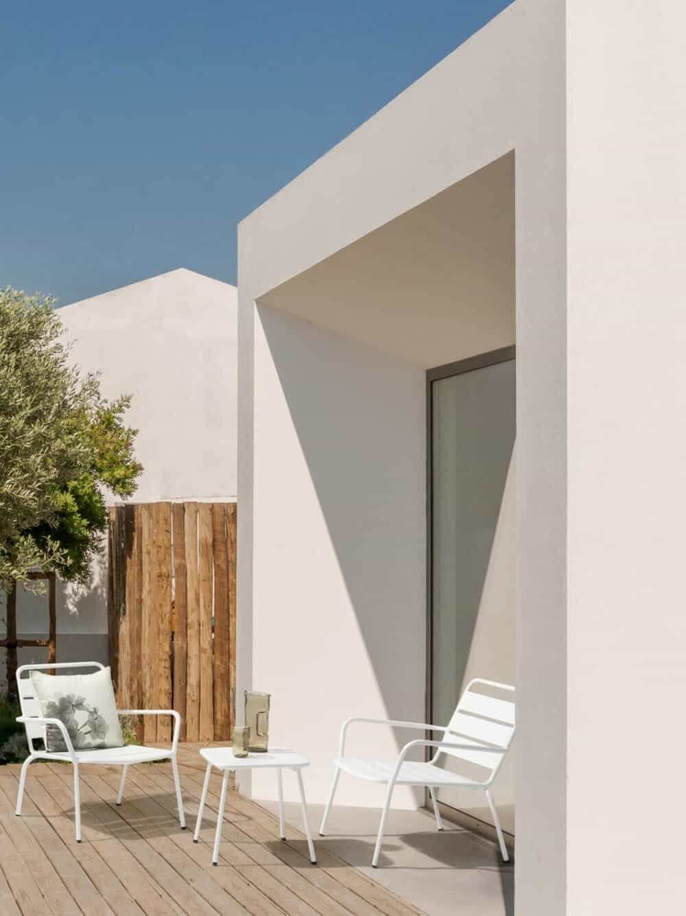 Sedia bianca moderna e tavolino su terrazza minimalista con pareti bianche e decorazioni.