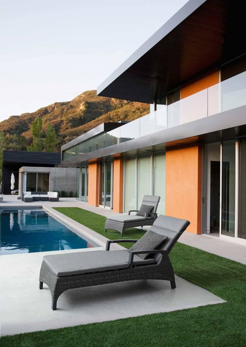 Esterni di casa moderna con piscina e lettini in rattan, ambienti di lusso e relax al sole.