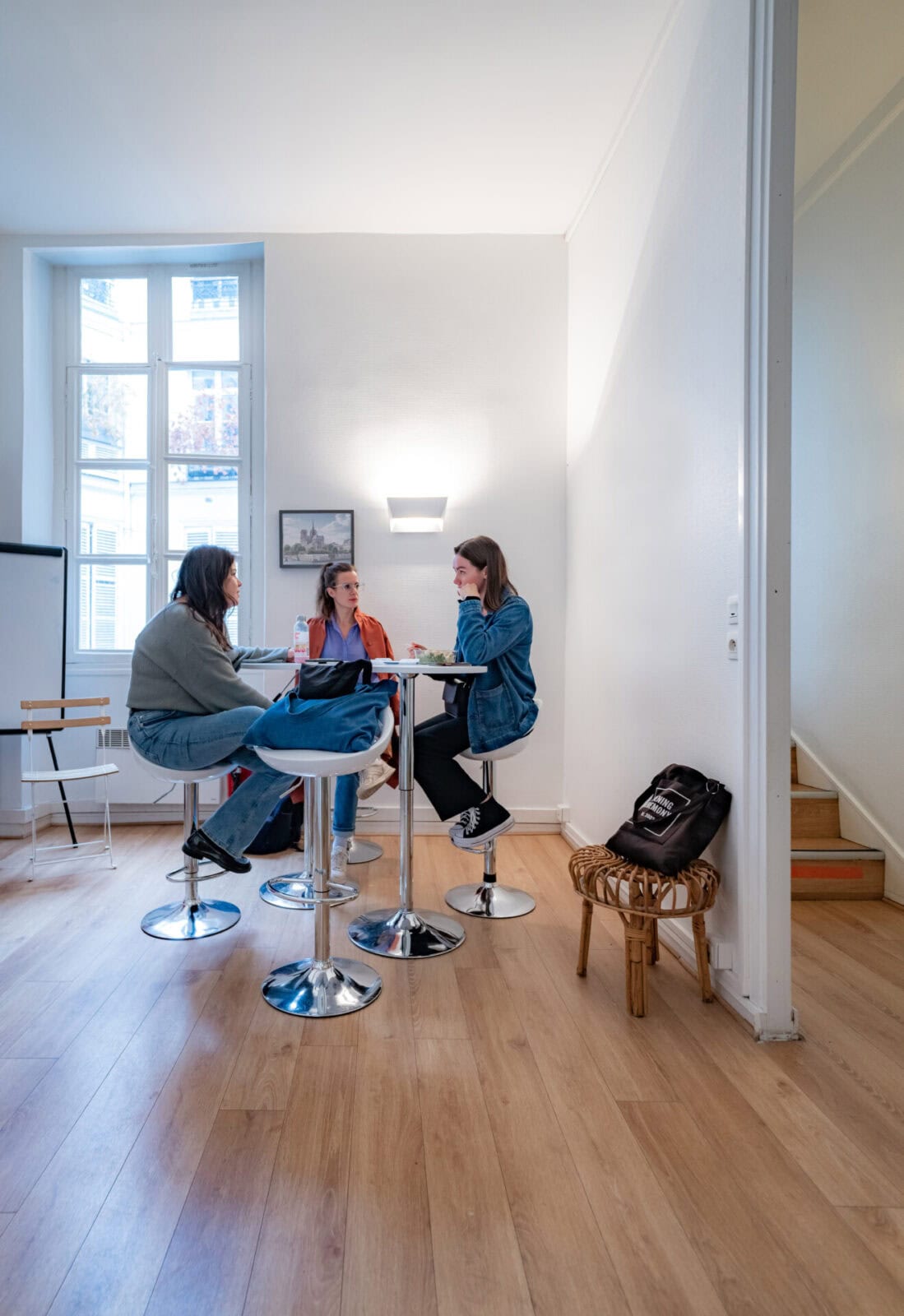 Drei junge Frauen sitzen an einem hohen Tisch in einem hellen Raum und unterhalten sich.