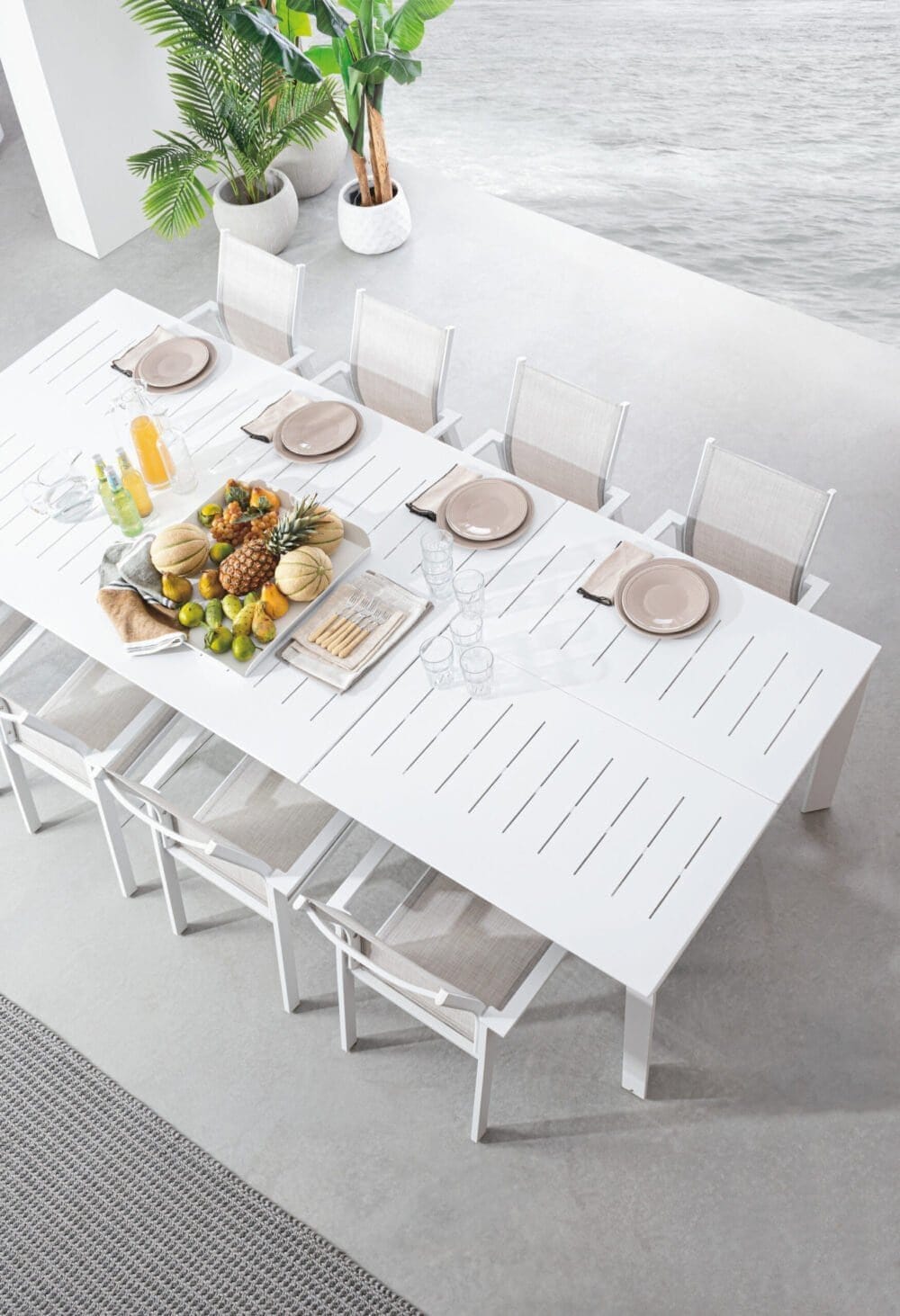 Immagine di un tavolo da pranzo bianco decorato con frutta e acqua, vista sul mare, stile moderno e minimalista.