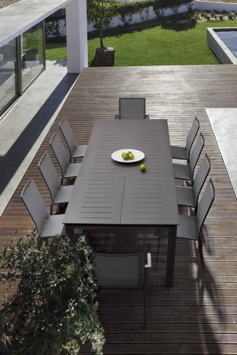 Tavolo all'aperto con sedie grigie, ambiente esterno elegante con piscina e giardino, ideale per pranzo o relax.