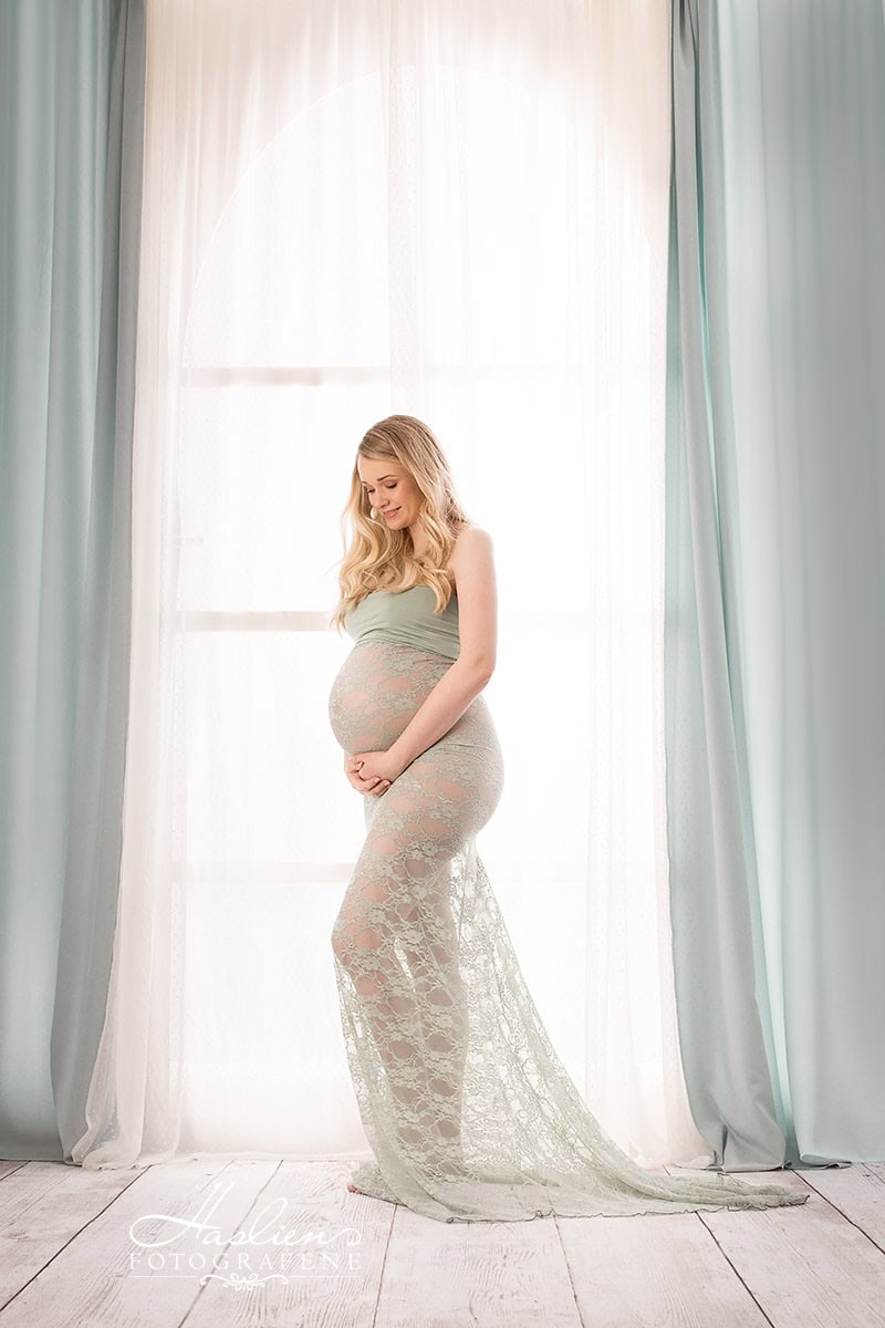 Kvinne som bærer graviditetsskjørt foran et lyst vindu i et studio, for gravidefotografering.