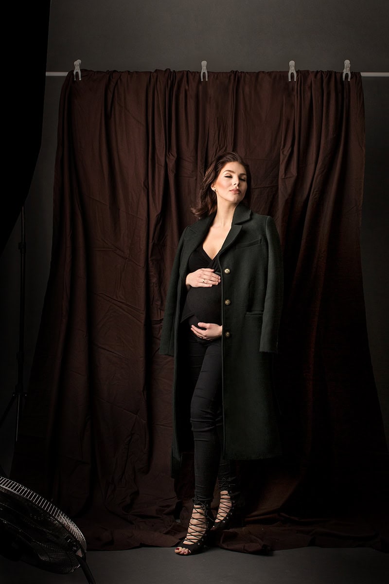 Elegant gravidfotografering med kvinnen i svart klær foran brunt bakteppe.