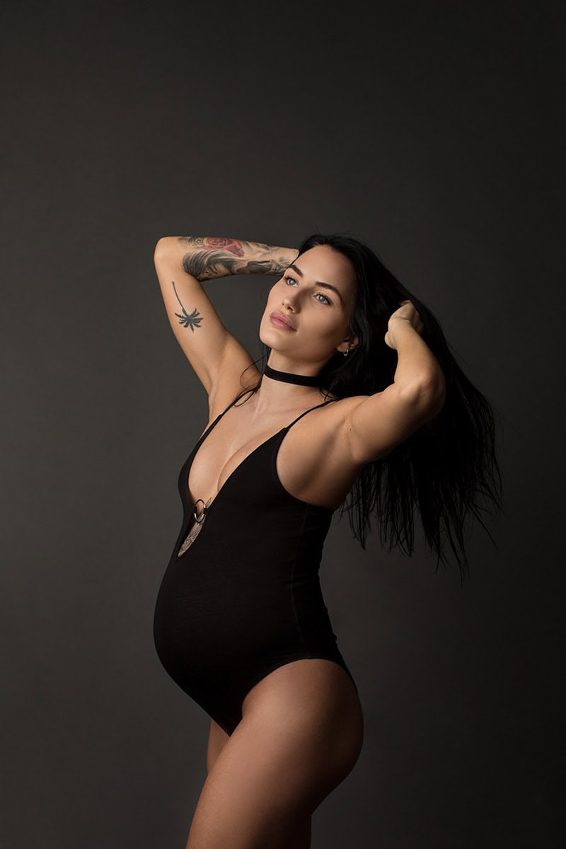 Kvinne med gravid mage i svart body og tattooer, portrettfotografering for gravide, kunstnerisk gravidfoto, mamatrykk og graviditetsposter, gravidfotografering i studio.