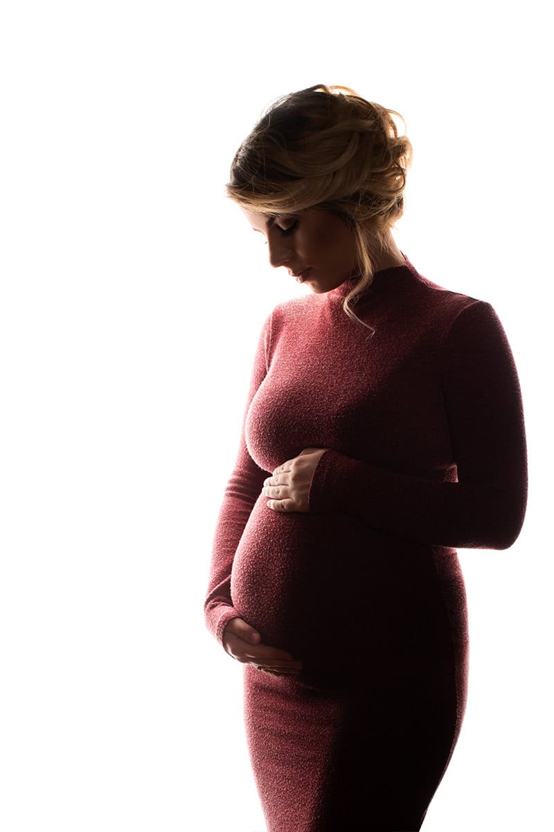 Elegant gravidfoto av gravide kvinne i profil, med fokus på magen, i myk belysning for naturlig og intim stemning. Perfekt for gravidefotoshoots og minneverdige øyeblikk.