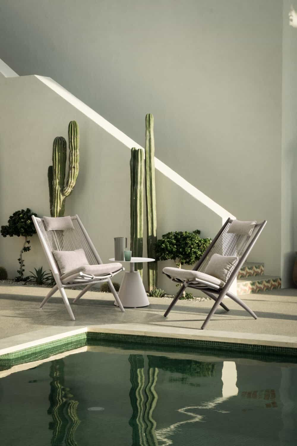 Poltrone in tessuto beige con cactus decorativi verdi sullo sfondo, ambiente esterno elegante e di design.