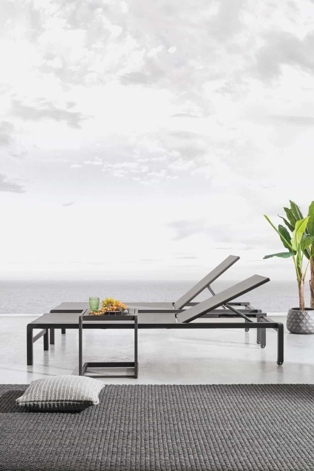Sdraio nere con tavolino e piante tropicali, relax fronte mare, ambiente elegante e moderno.