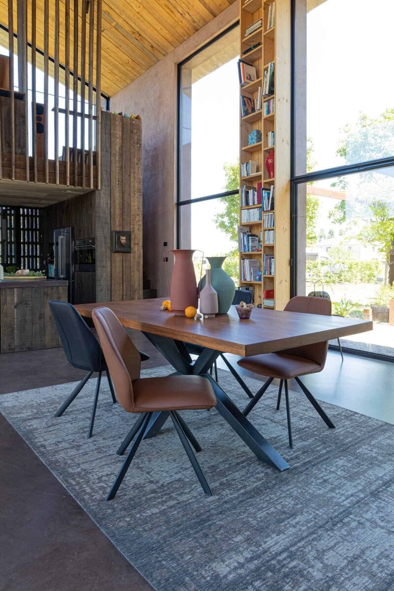 Ampia sala da pranzo moderna con tavolo in legno e sedie di design, grandi finestre e libreria alta, luminoso e accogliente.