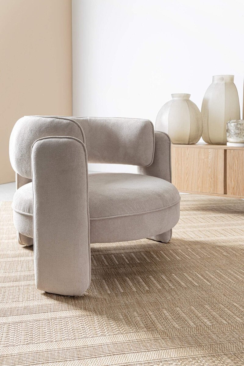 Poltrona in tessuto beige con design minimalista e comfort, perfetta per ambienti eleganti.