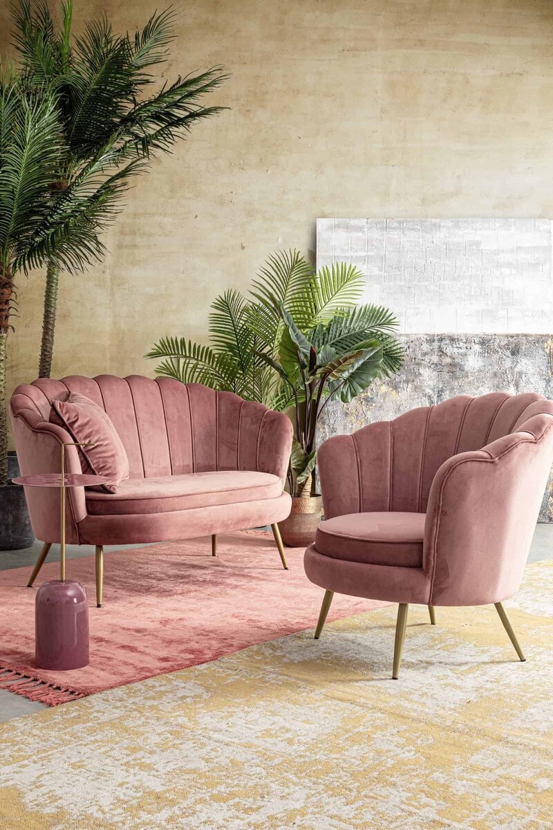 Alt text: Divani in velluto rosa con mobili di design, piante verdi, atmosfera di lusso moderna.