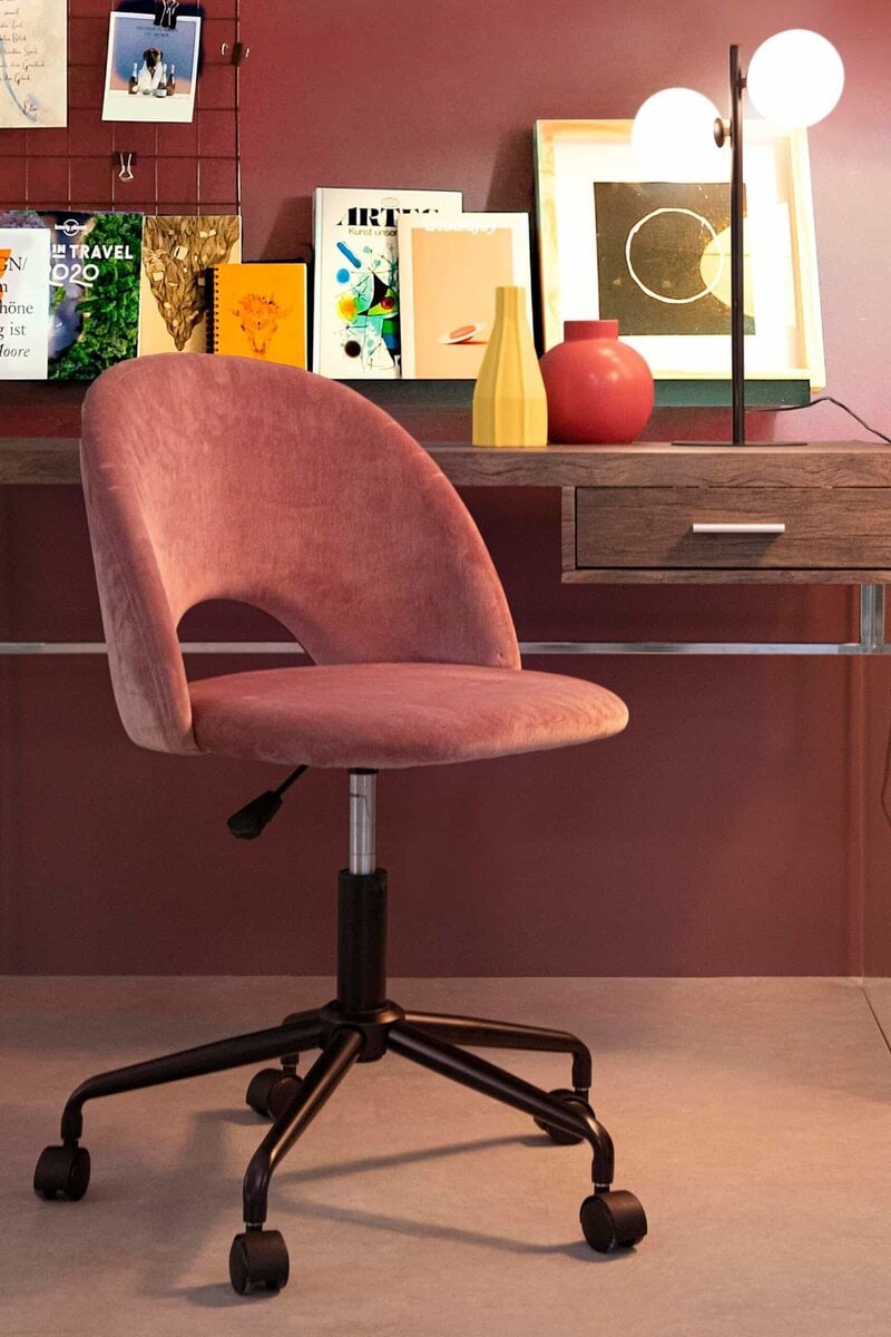 Alt text: Sedia rosa in velluto con schienale curvo, scrivania con decorazioni colorate e lampada moderna.