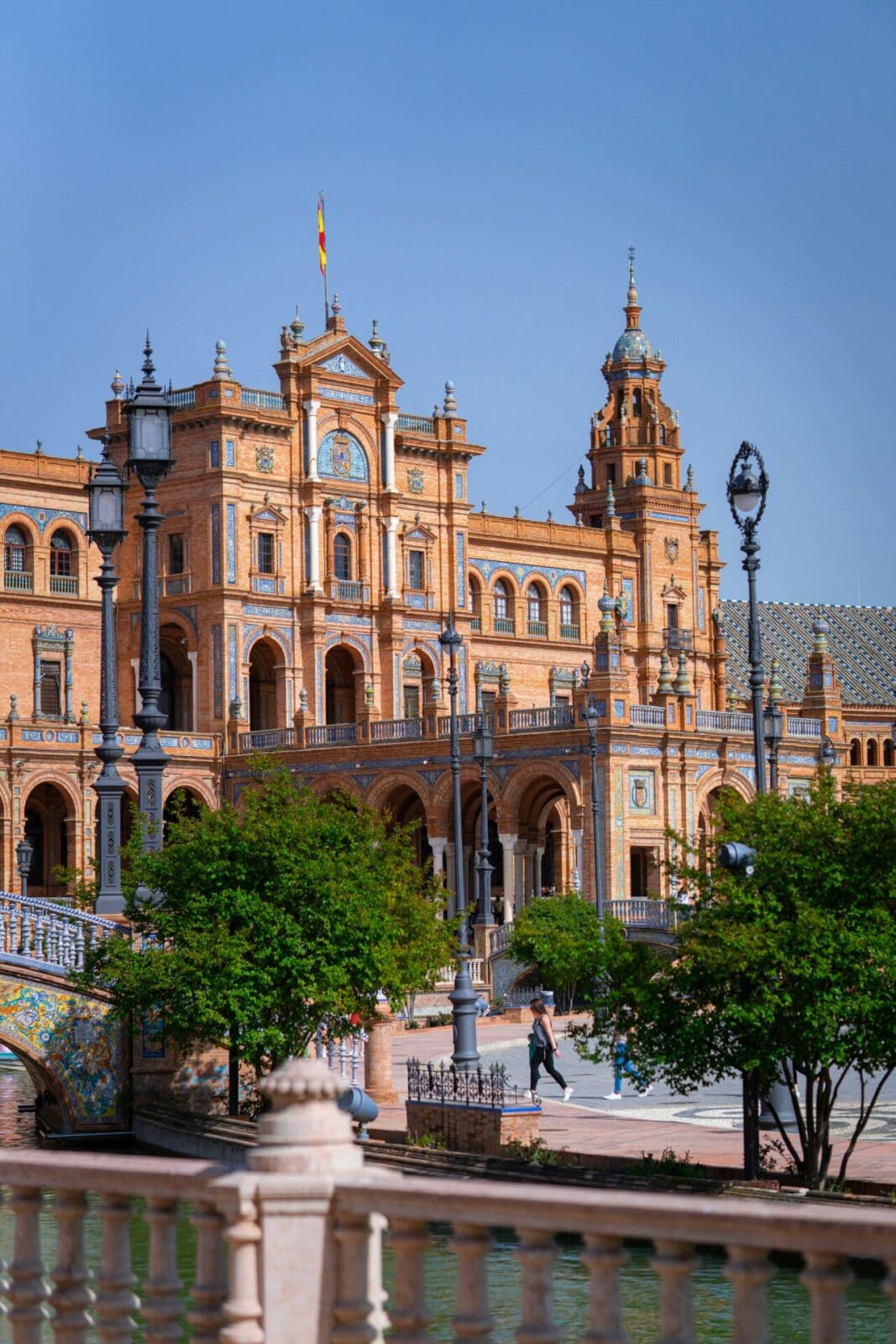 Blick auf die Plaza de España in Sevilla mit beeindruckender Architektur, bunten Keramikdetails und Menschen im Vordergrund.