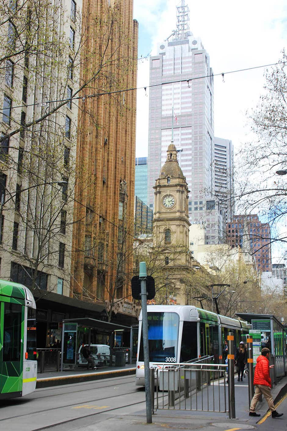Straßenszene in Melbourne mit historischen und modernen Gebäuden sowie den ikonischen Straßenbahnen.