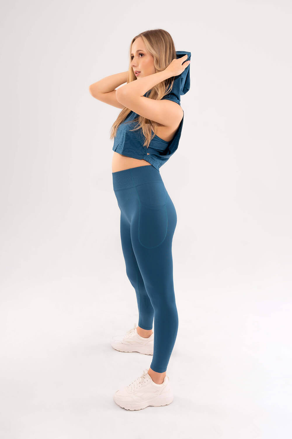 mujer de perfil luce blusa con capucha y leggins deportivo con bolsillos color azul verdoso oscuro