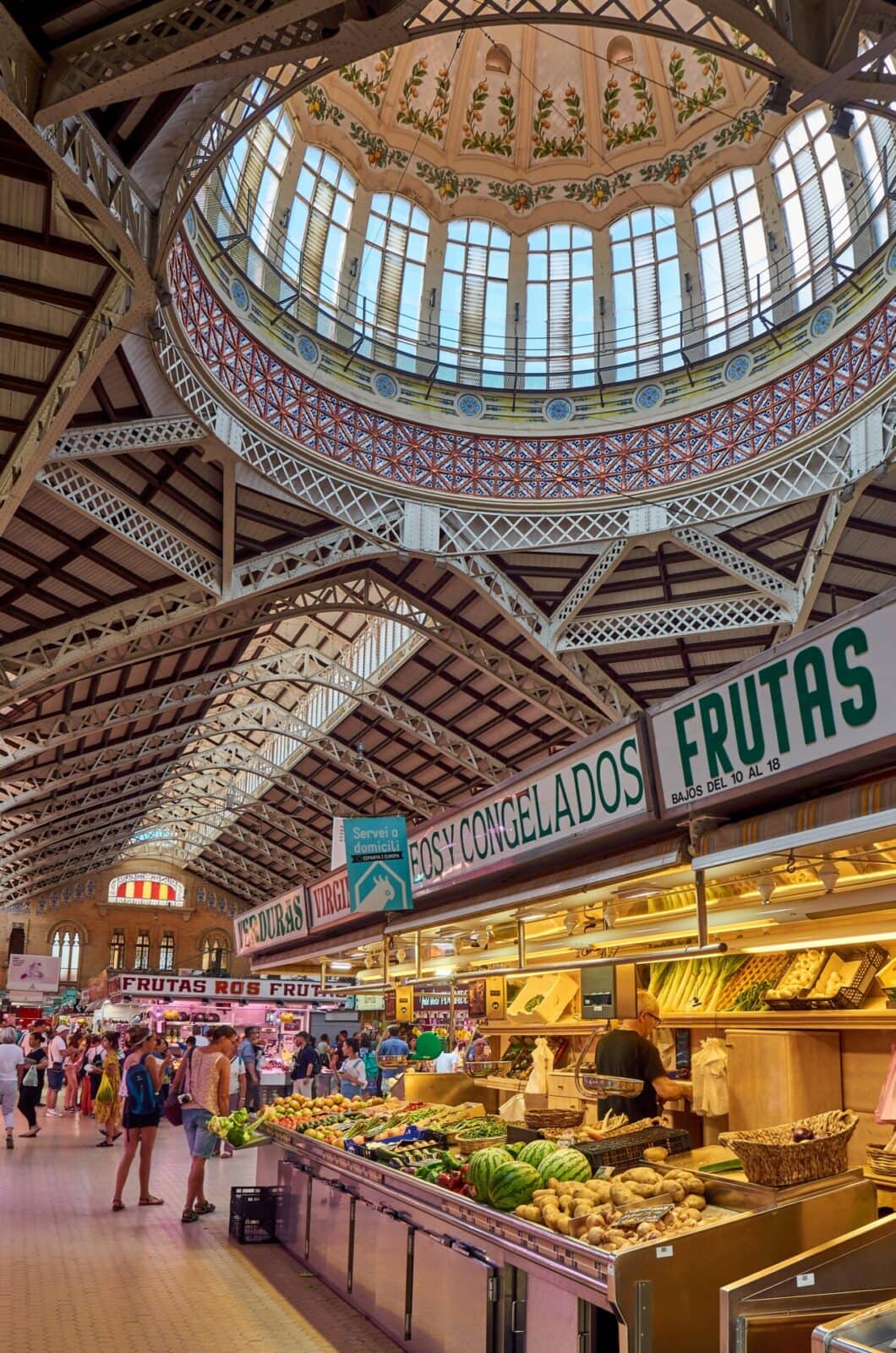 Historische Markthalle mit kunstvoller Glaskuppel und buntem Gemüse- und Obststand in Valencia.