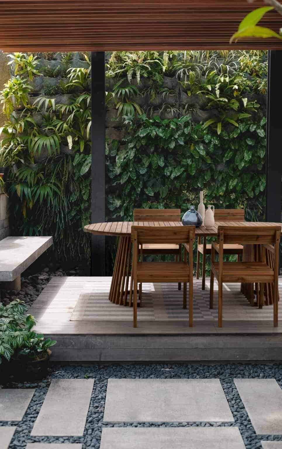 Tavolo in legno e panchine in un giardino pieno di piante verdi e fiori, ambiente naturale e accogliente.