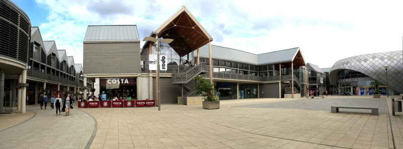 Modernes Einkaufszentrum mit Costa Coffee und Debenhams, offener Platz mit Sitzmöglichkeiten und Passanten.