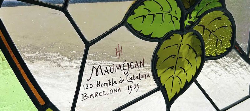 Detail eines historischen Jugendstil-Buntglasfensters von Mauméjean aus dem Jahr 1909 in Barcelona mit kunstvollen Blattmotiven.