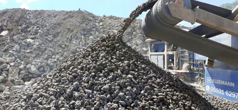 Steine werden von einem Förderband auf einen Steinhaufen befördert, auf einer Baustelle