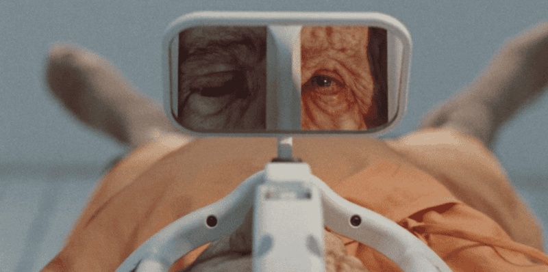 “Close-up of an elderly person’s reflection in a medical mirror, evoking themes of mortality, cloning, and distorted identity.”