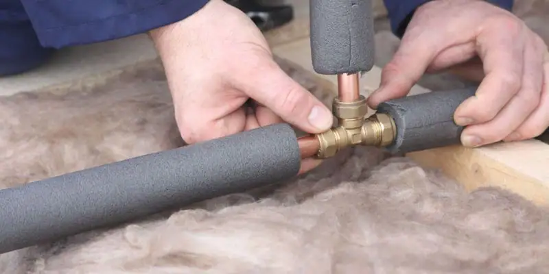 pipe insulation - Man fixing foam insulation to a water pipe - person installing foam pipe insulation on copper pipes