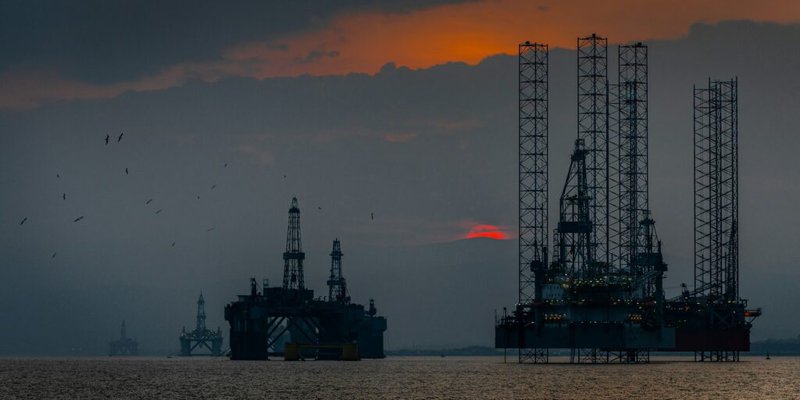 Silhouette of offshore oil and gas rigs at sunset, illustrating hard-to-abate industrial sectors that require both decarbonization and carbon capture solutions.