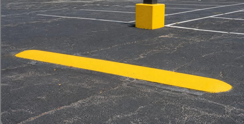 Yellow-painted concrete light pole base in an asphalt parking lot