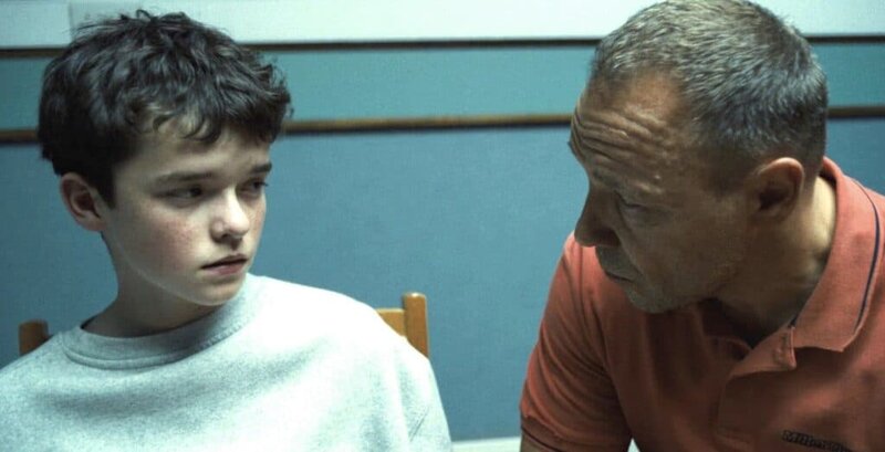 Scene from Netflix series Adolescence showing a young boy and his father seated in a police interrogation room, conveying tension and emotional gravity.