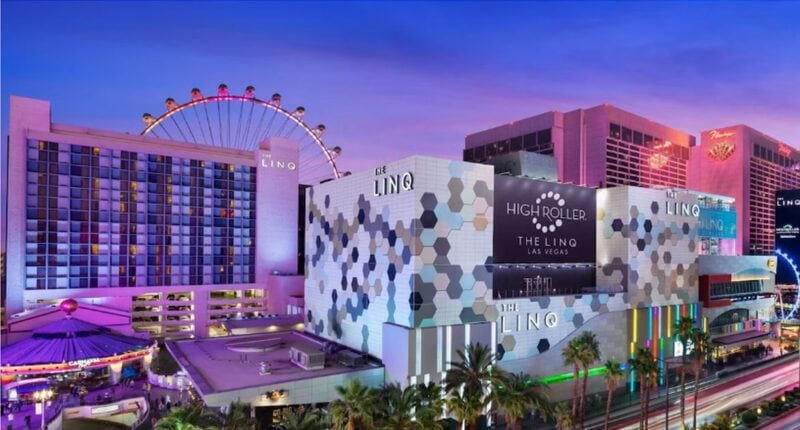 Exterior view of The LINQ Hotel & Casino in Las Vegas featuring illuminated signage, modern geometric facade, and the High Roller observation wheel lit up in pink at twilight.