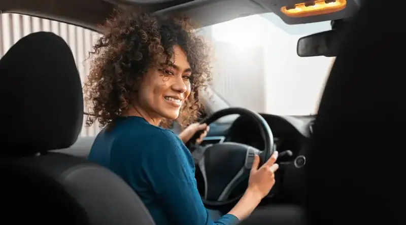 Mulher jovem sorridente ao volante para ilustrar o artigo sobre CNH digital