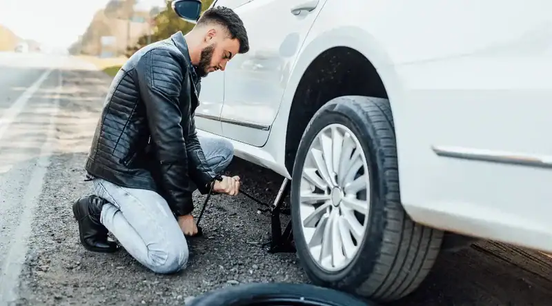 Imagem de um homem trocando o pneu do carro para ilustrar o artigo sobre kit de ferramentas de emergência para carros.