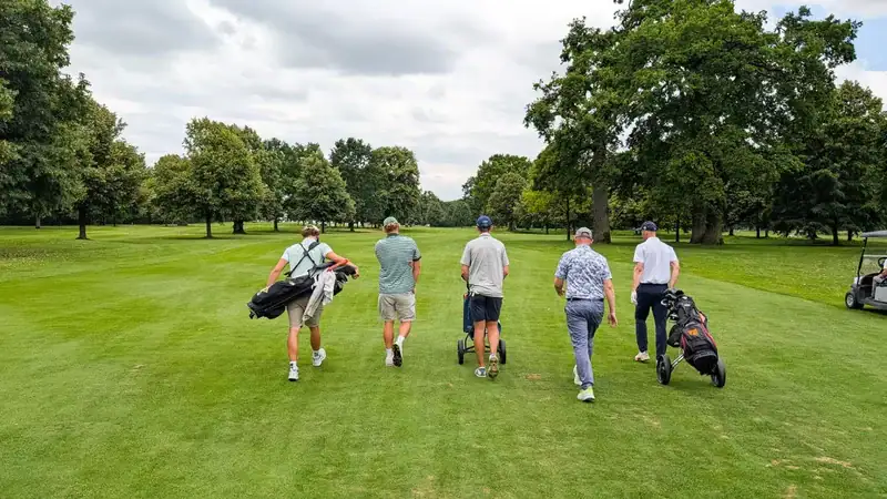 Fünf Golfer gehen mit ihrer Ausrüstung über einen grünen Golfplatz