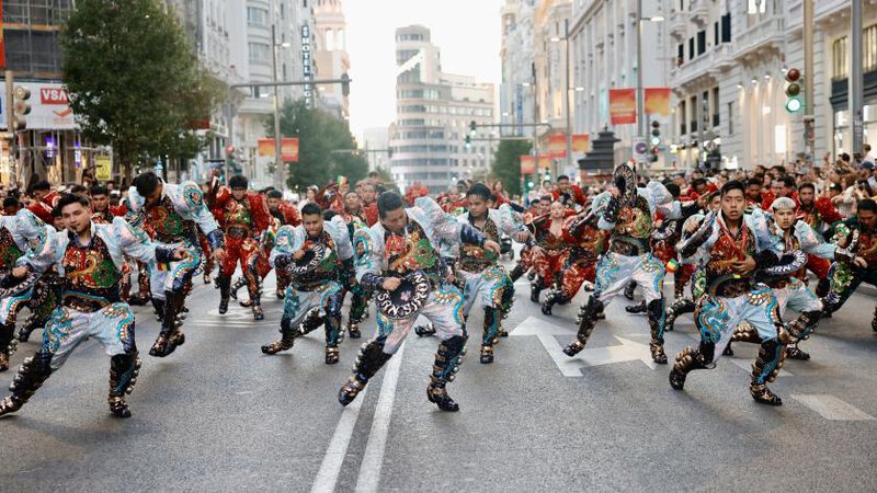 Grupo de bailarines en trajes coloridos realizando una coreografía en una calle de Madrid durante un desfile.