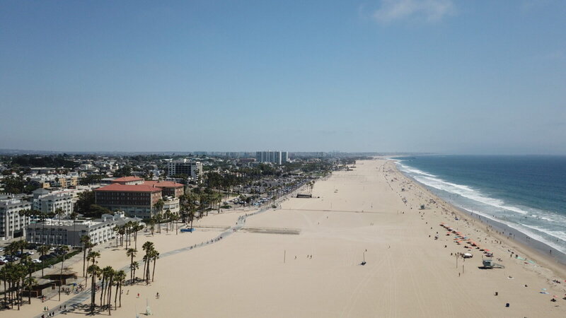 Luftaufnahme des Santa Monica Beach in Los Angeles mit Sandstrand, Pazifik und Palmen unter klarem Himmel.