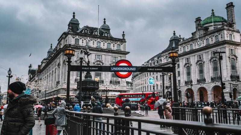 Piccadilly Circus in London mit U-Bahn-Eingang, roten Doppeldeckerbussen und historischen Gebäuden.