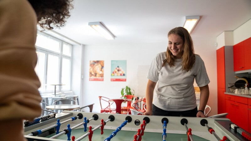 Lachende Frau spielt Tischfußball in einer freundlichen Gemeinschaftsküche mit modernem Design.