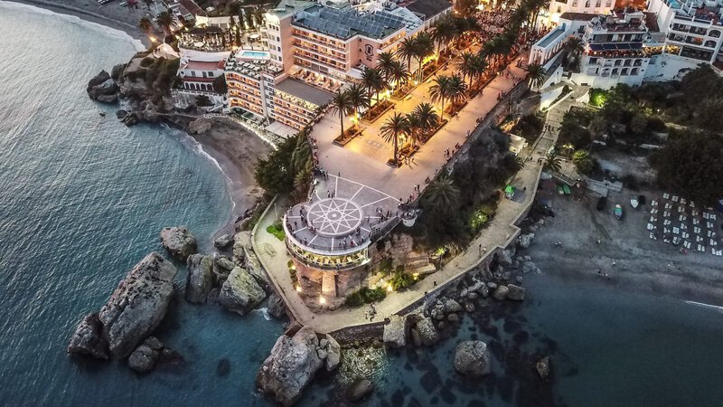 Abendliche Luftaufnahme vom Balcón de Europa in Nerja mit beleuchteter Promenade, Palmen und umliegenden Stränden