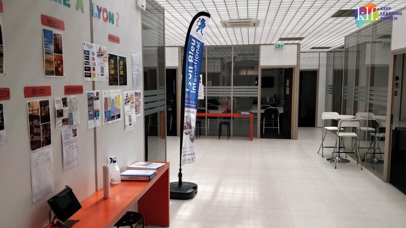 Moderner Aufenthaltsbereich der Sprachschule Lyon Bleu International mit Infowand und Sitzmöglichkeiten.