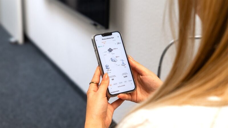 Abbildung einer Person mit Smartphone in der Hand. Auf dem Smartphone ist die Energie-App der PV-Anlage abgebildet.