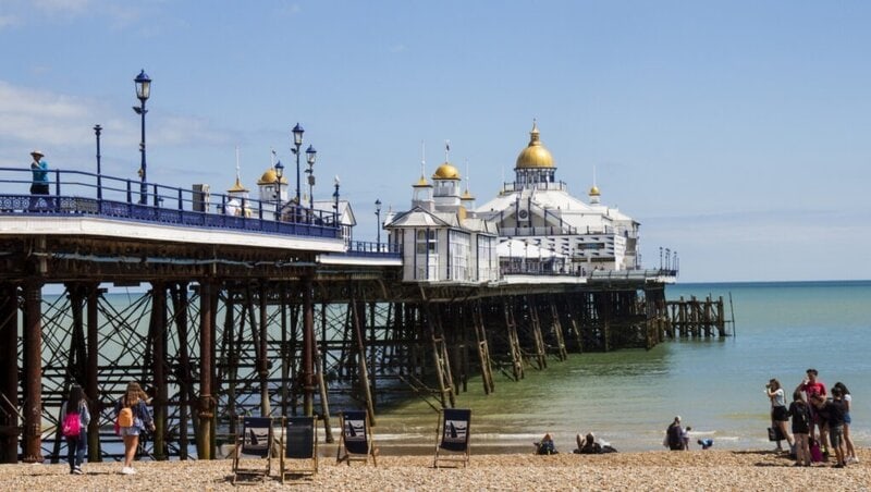 Der historische Eastbourne Pier mit seinen goldenen Kuppeln und viktorianischer Architektur, umgeben von Strandbesuchern.