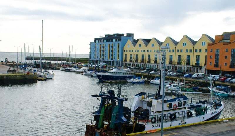 Fischerboote und Yachten im Hafen von Galway, Irland, mit bunten Gebäuden im Hintergrund.