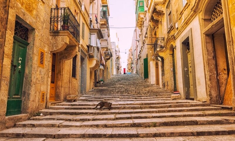 Malerische, historische Treppenstraße in Valletta, Malta, mit bunten Balkonen und alten Sandsteinhäusern.