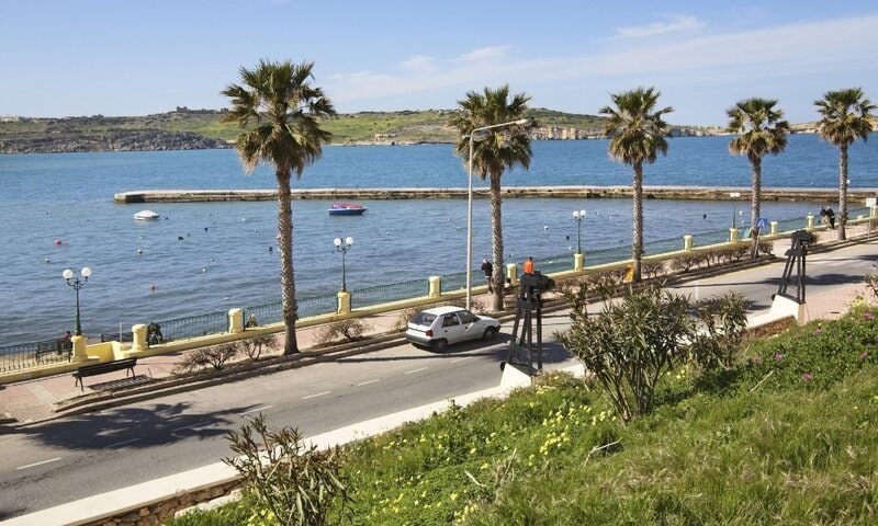 Palmen gesäumte Küstenpromenade mit Blick auf das blaue Mittelmeer und eine ruhige Bucht.