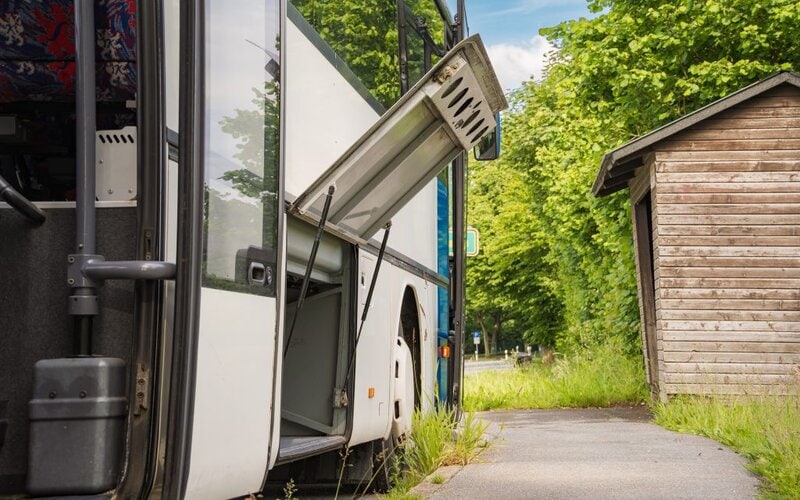 Bequemer Ausflugsbus der Ambos GmbH in einer Haltestellenbucht mit geöffnetem Kofferraum.