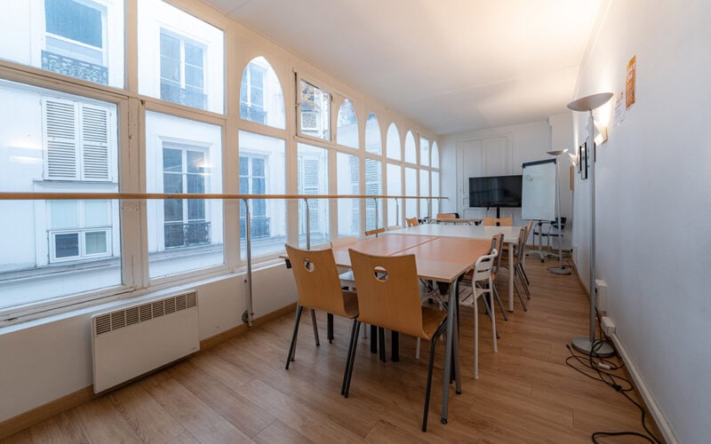 Heller Konferenzraum mit großen Fenstern, Holzboden, Tischen und moderner Ausstattung.